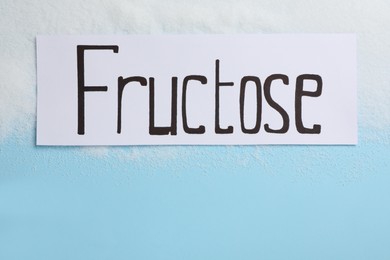 Photo of Paper with word Fructose and sugar on light blue background, flat lay. Space for text