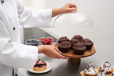 Female pastry chef with tasty cupcakes at table in kitchen, closeup