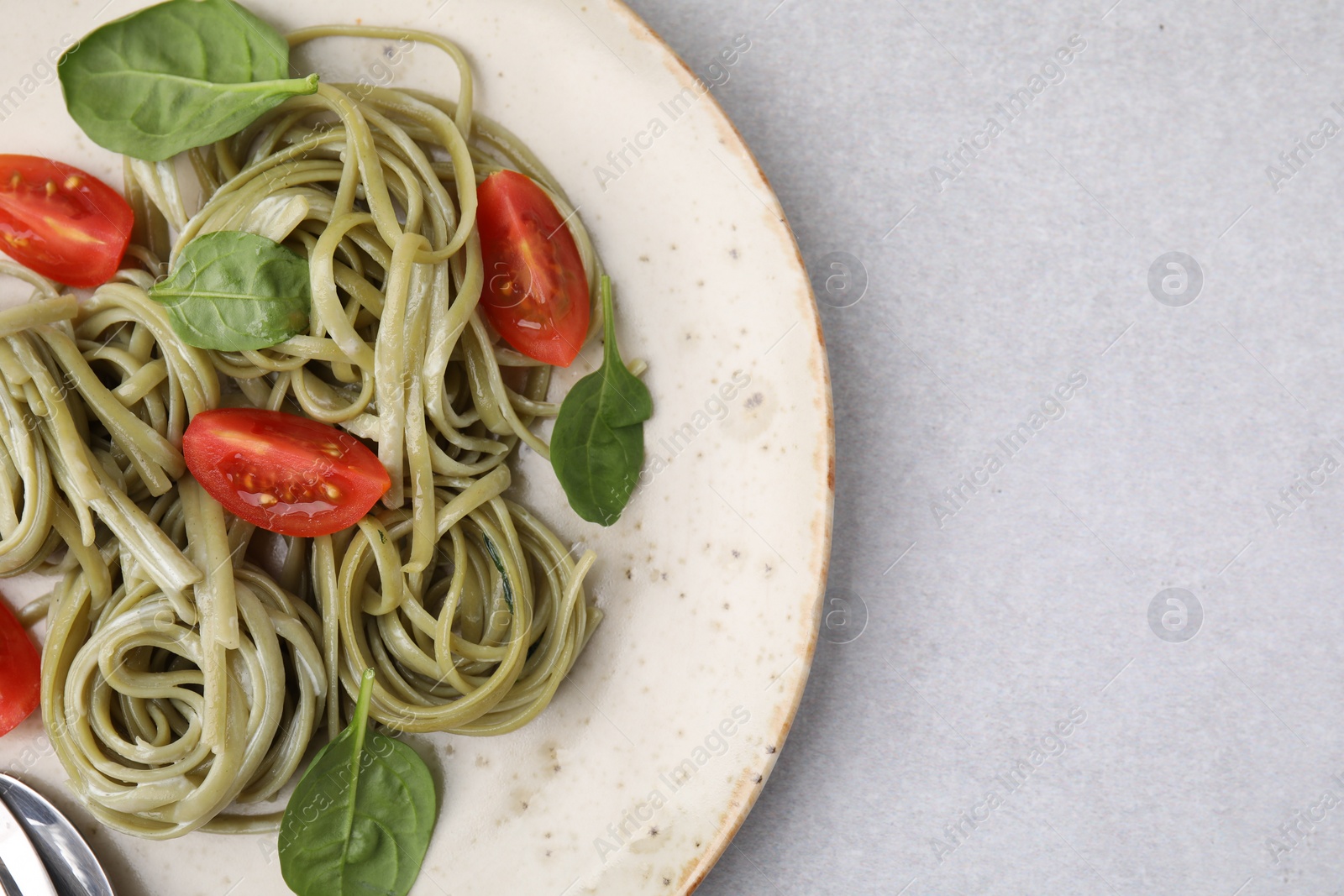 Photo of Tasty pasta with spinach and tomatoes on light grey table, top view. Space for text