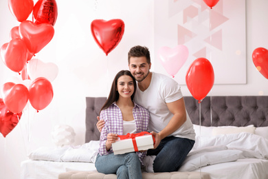 Photo of Happy young couple in bedroom decorated with heart shaped balloons. Valentine's day celebration