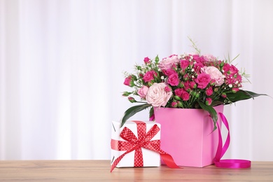 Photo of Beautiful bouquet of flowers and gift box on table against light background. Space for text