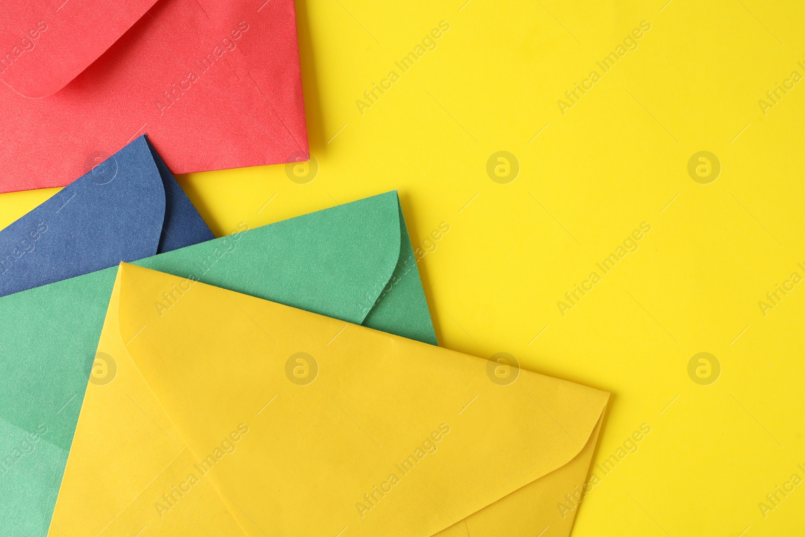Photo of Colorful paper envelopes on yellow background, top view. Space for text