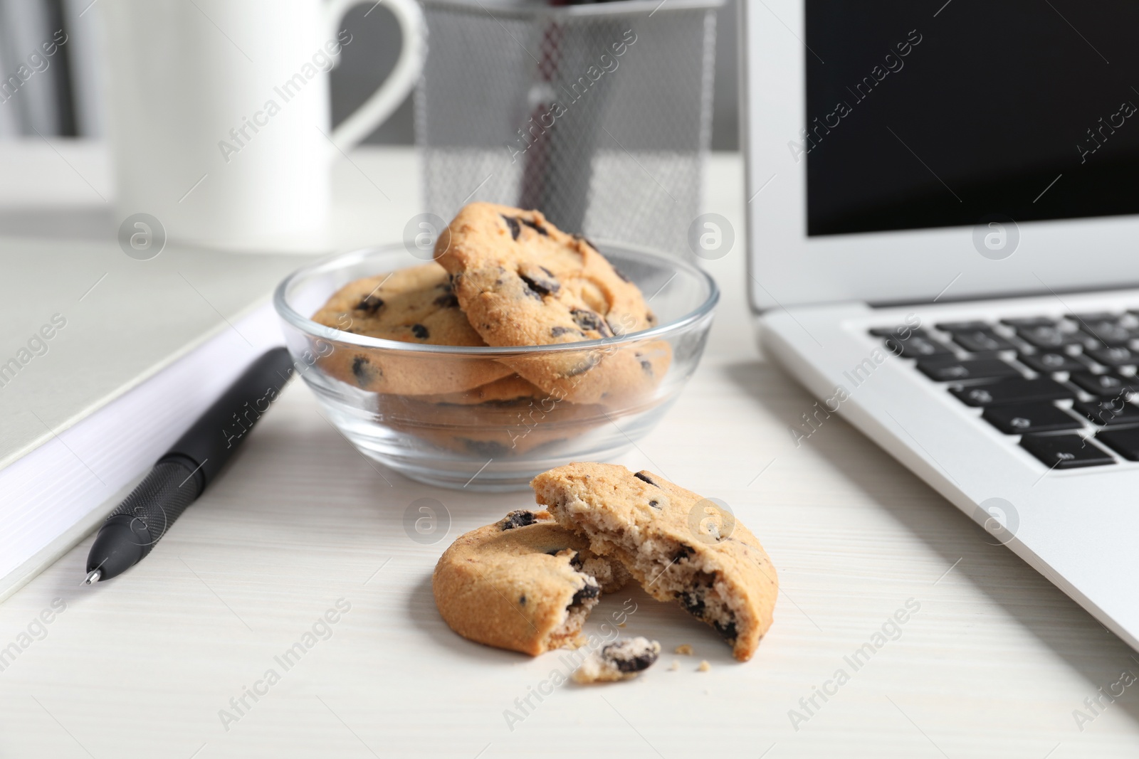 Photo of Chocolate chip cookies and laptop on white wooden table in office