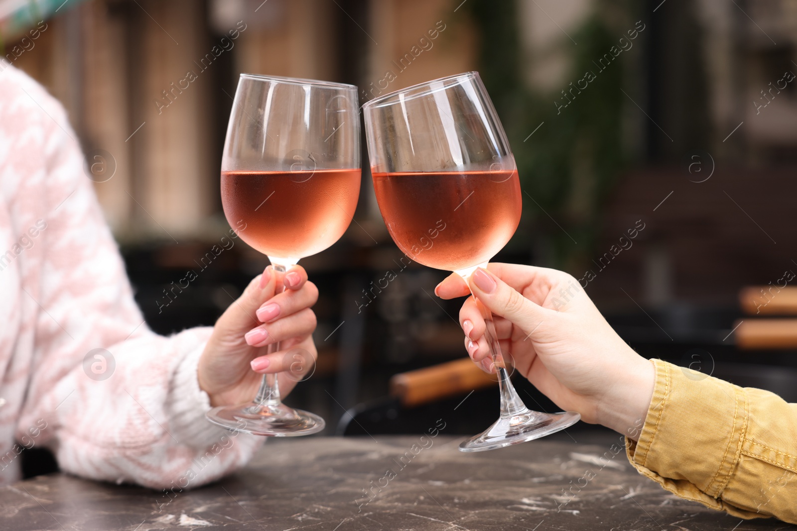 Photo of Women clinking glasses with rose wine at dark marble table in outdoor cafe, closeup