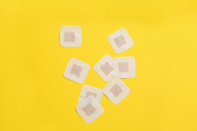 Photo of Sticking plasters on yellow background, flat lay