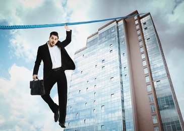Image of Risks and challenges of entrepreneurship. Businessman with portfolio holding on to rope leading to top of building