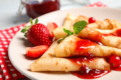 Delicious thin pancakes with strawberries and jam on plate, closeup