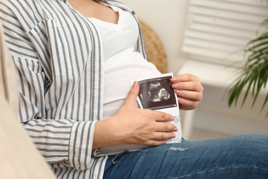 Photo of Pregnant woman with ultrasound photo of her baby at home, closeup