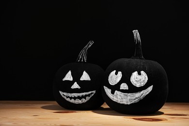 Halloween pumpkins with drawn faces on wooden table against black background, space for text