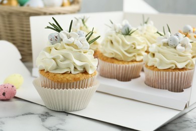 Tasty Easter cupcakes with vanilla cream on white marble table