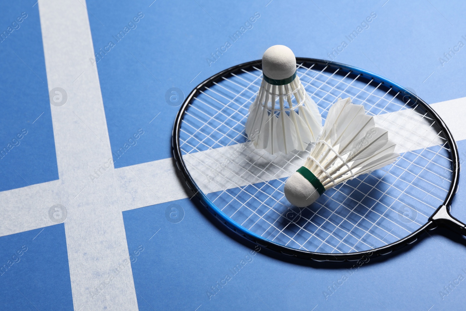 Photo of Feather badminton shuttlecocks and racket on blue background. Space for text