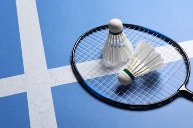 Feather badminton shuttlecocks and racket on blue background. Space for text