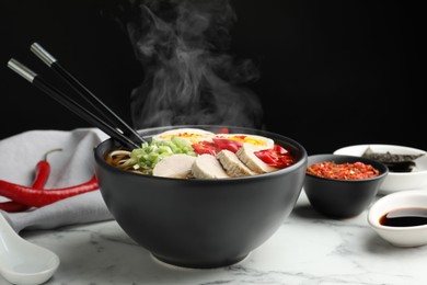 Image of Delicious hot ramen in bowl on white marble table against black background, closeup. Noodle soup