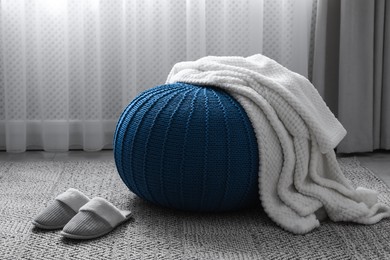 Photo of Soft blanket on stylish blue pouf and slippers in room