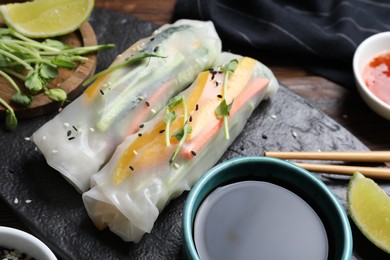 Tasty spring rolls, soy sauce, sesame seeds and microgreens on table, closeup