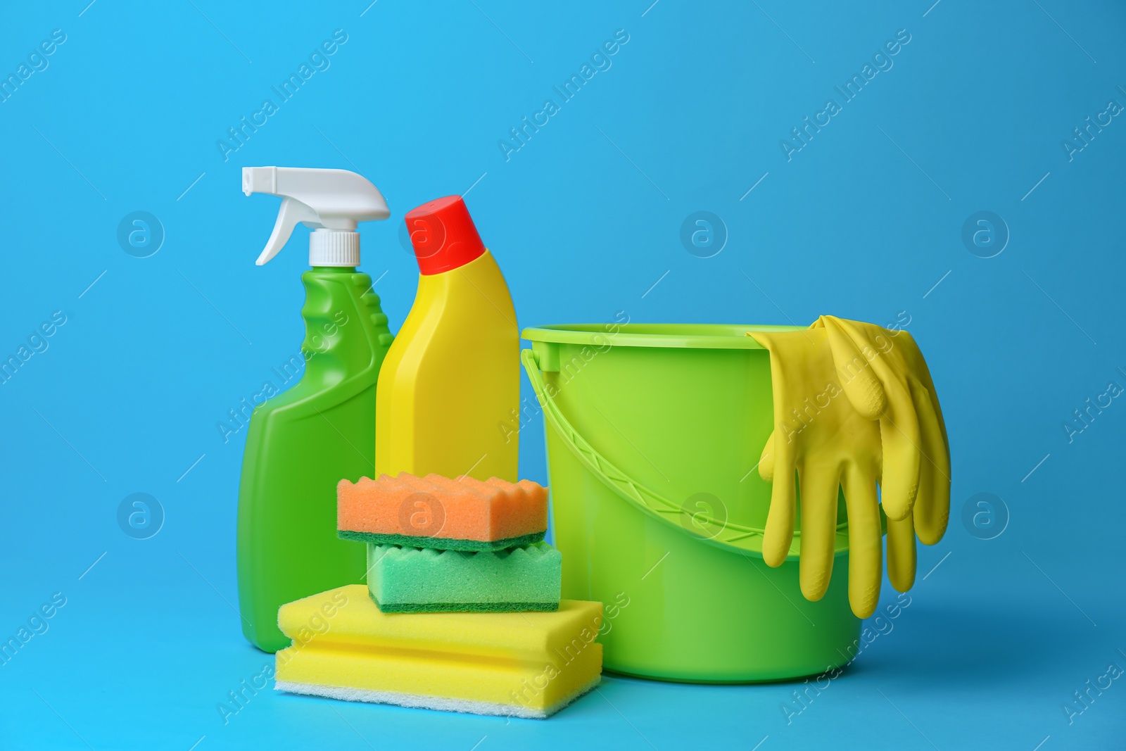 Photo of Green bucket, cleaning supplies and tools on light blue background