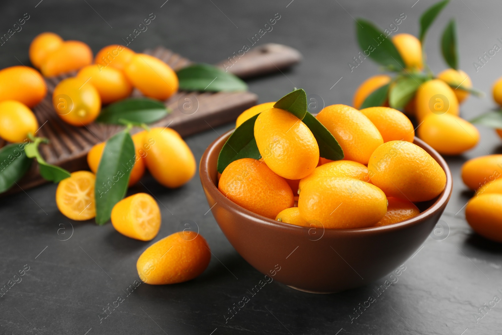 Photo of Fresh ripe kumquats in bowl on black table