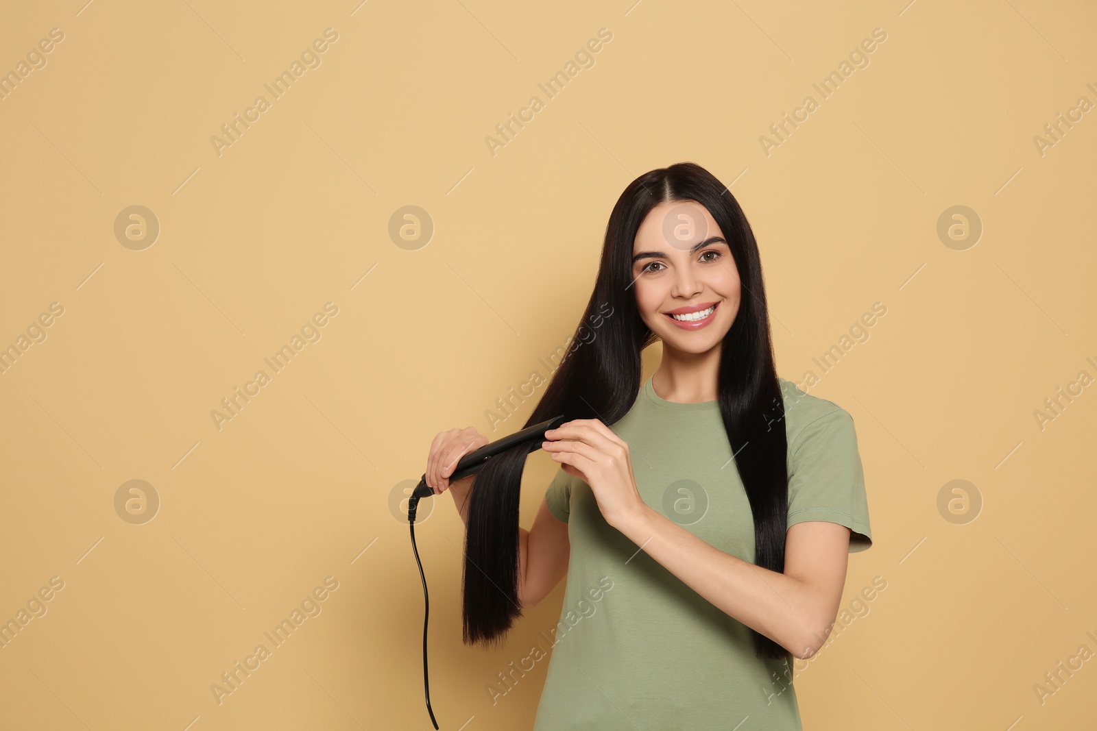 Photo of Beautiful happy woman using hair iron on beige background. Space for text