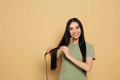 Beautiful happy woman using hair iron on beige background. Space for text