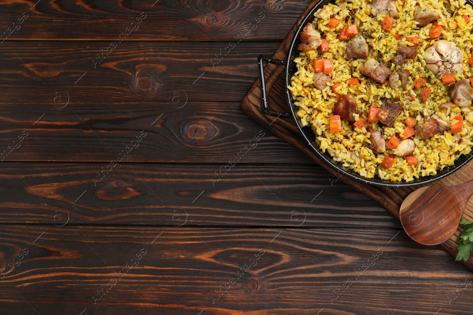 Photo of Delicious pilaf with meat, carrot and garlic served on wooden table, top view. Space for text