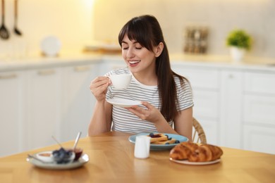 Smiling woman drinking coffee at breakfast indoors