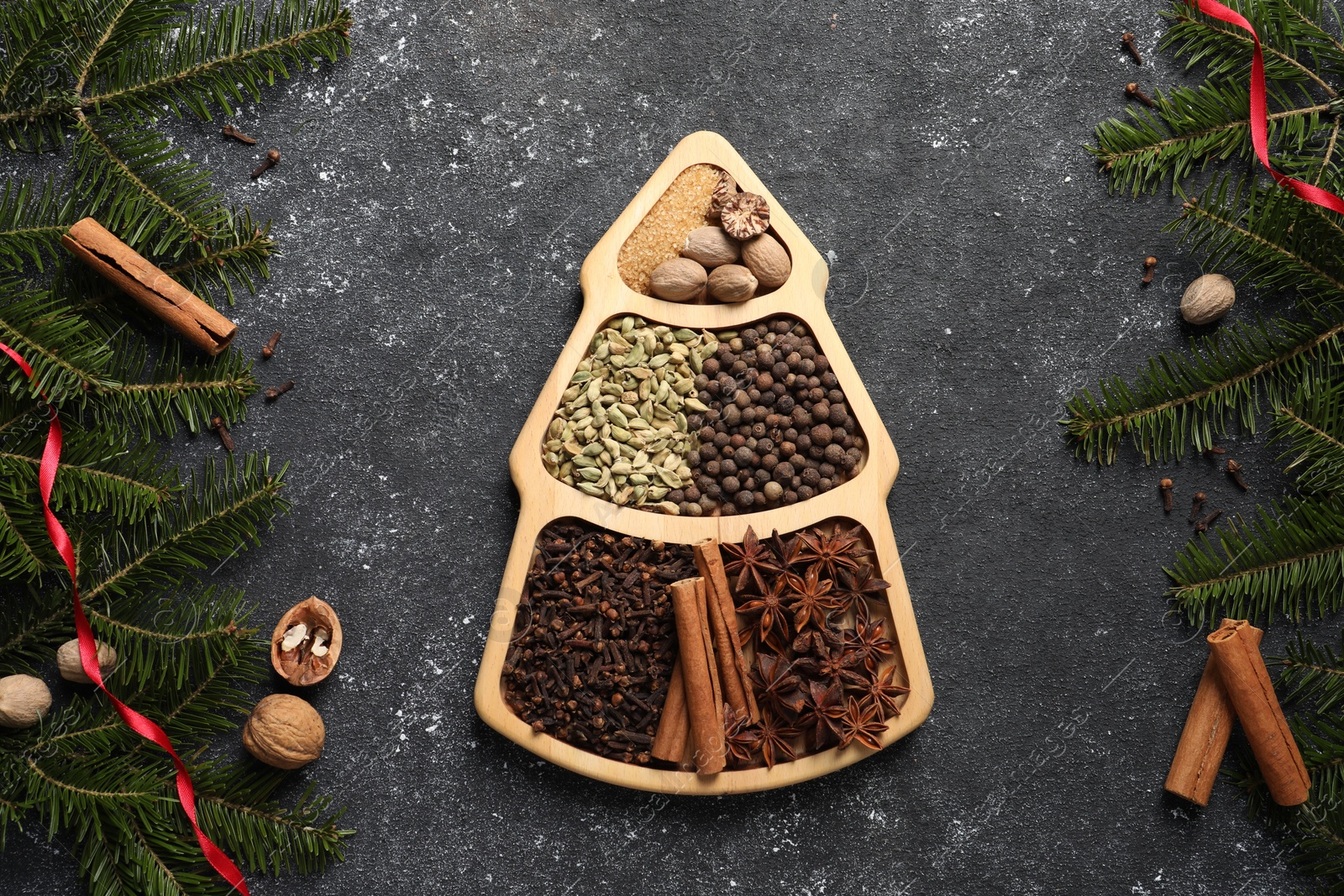 Photo of Different spices, nuts and fir branches on dark gray textured table, flat lay