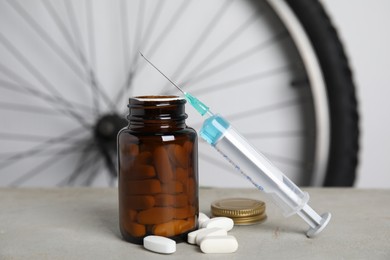 Photo of Pills and syringe on light grey table near bike wheel. Using doping in cycling sport concept