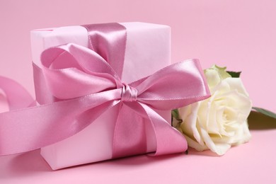 Photo of Gift box and beautiful rose flower on pink background, closeup