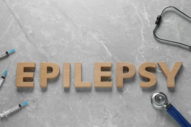 Photo of Word Epilepsy made of wooden letters, stethoscope and syringes on grey marble table, flat lay