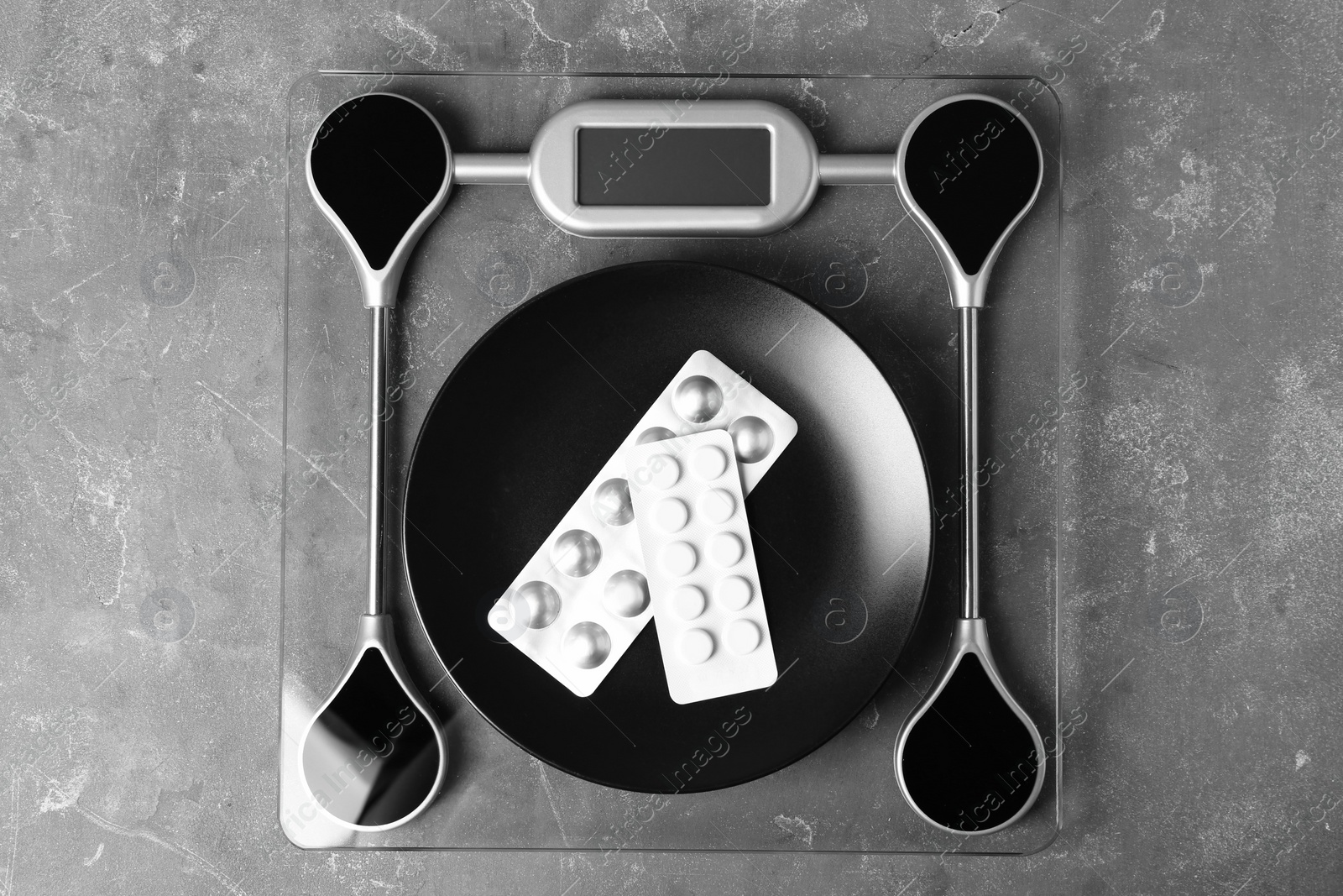 Photo of Scales with plate of weight loss pills  in blister packs on gray background, top view