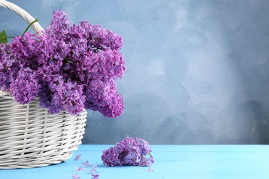 Photo of Beautiful lilac flowers in wicker basket on light blue wooden table, space for text