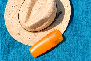 Photo of Stylish straw hat and bottle of sunblock on soft blue beach towel, flat lay