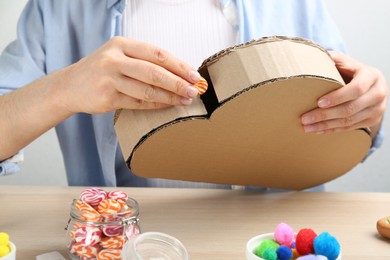 Photo of Woman putting candy in cardboard cloud at wooden table, closeup. Pinata diy
