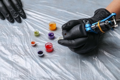 Photo of Tattoo artist with machine and inks at table, closeup