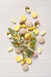 Photo of Different pills, herbs and flowers on white wooden table, flat lay. Dietary supplements