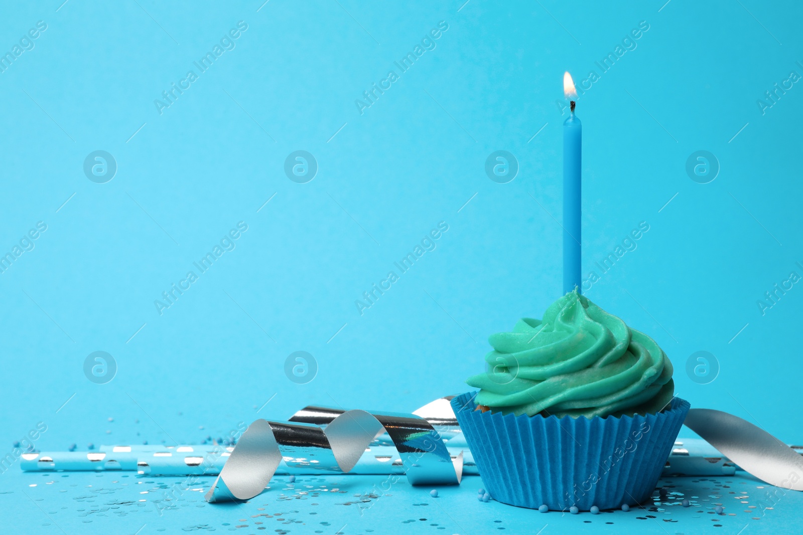 Photo of Delicious birthday cupcake with turquoise cream and burning candle on light blue background. Space for text