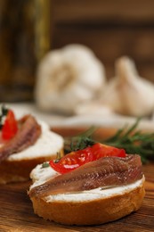 Delicious sandwiches with cream cheese, anchovies and tomatoes on wooden board, closeup. Space for text