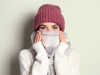 Photo of Young woman wearing warm sweater, scarf and hat on light background. Winter season