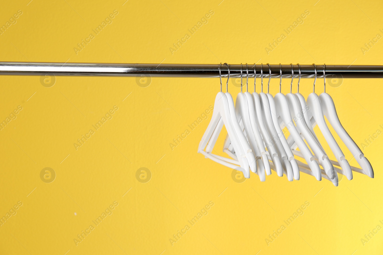 Photo of Metal rack with clothes hangers on color background, space for text