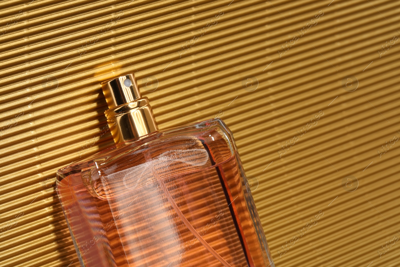 Photo of Luxury women's perfume. Sunlit glass bottle on golden surface, top view. Space for text