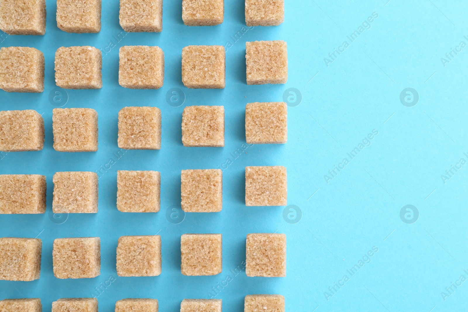 Photo of Brown sugar cubes on light blue background, top view. Space for text