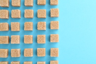 Photo of Brown sugar cubes on light blue background, top view. Space for text