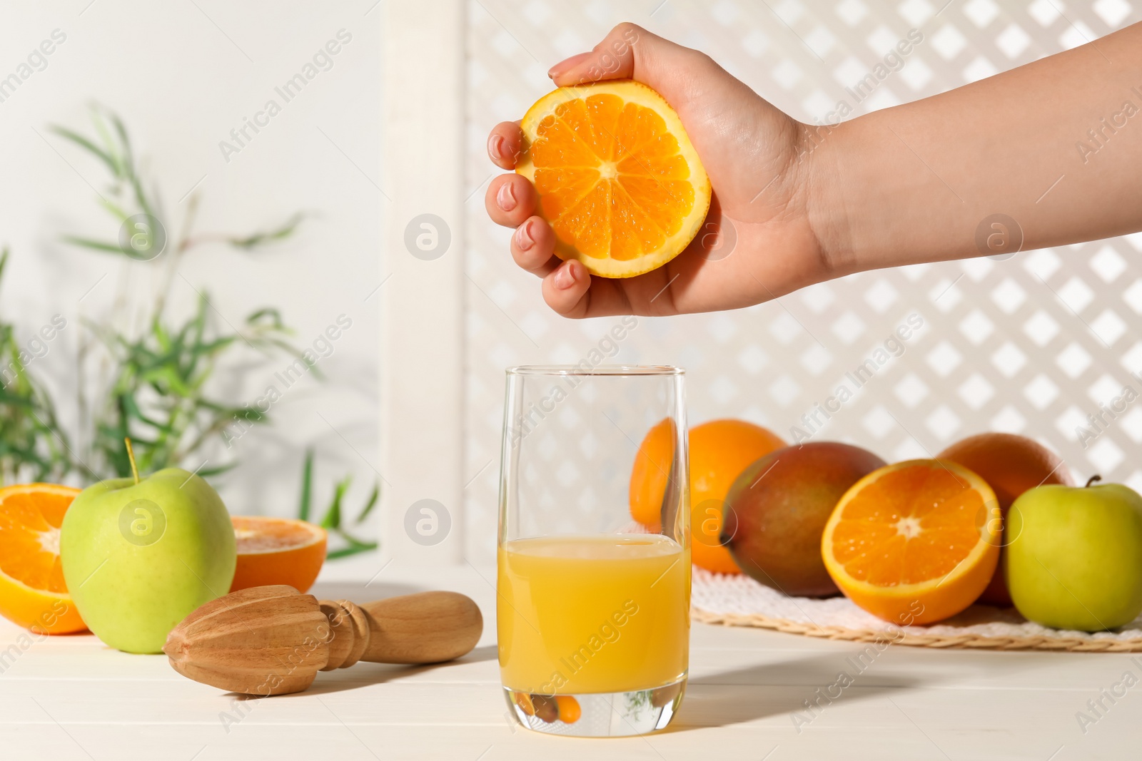 Photo of Woman squeezing orange over glass of juice at white wooden table, closeup