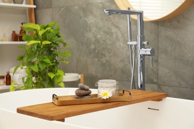 Photo of Shelving unit and wooden tub tray with different spa products in bathroom