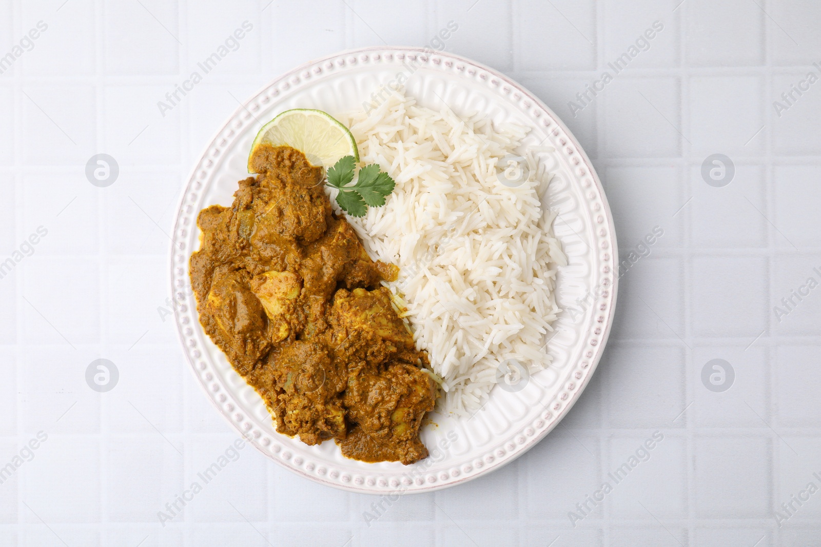 Photo of Delicious chicken curry with rice on white tiled table, top view