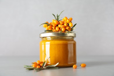 Photo of Delicious sea buckthorn jam and fresh berries on grey table