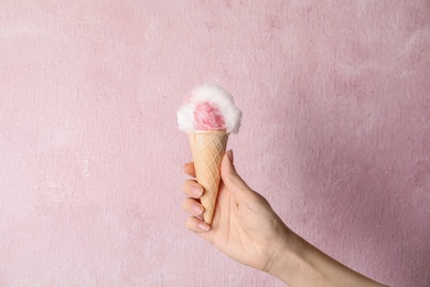 Photo of Woman holding ice cream cone with fluffy cotton candy on color background, closeup