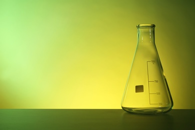 Photo of Empty conical flask on table against color background. Chemistry laboratory glassware