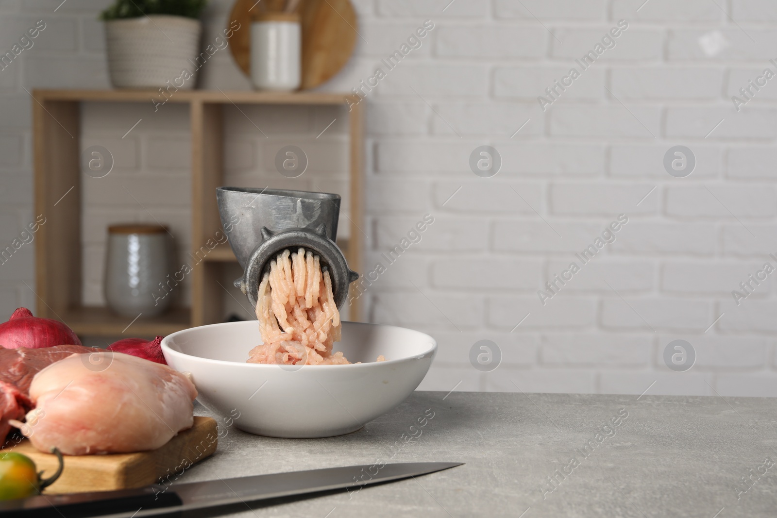 Photo of Metal meat grinder with chicken mince and products on light grey table indoors. Space for text