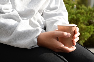 Photo of Woman sitting with cardboard cup of coffee outdoors, closeup
